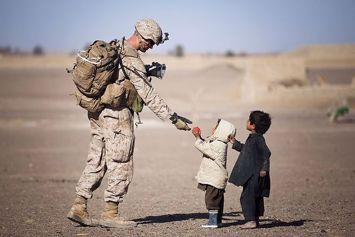 Marinesharingamomentwithlocalchildreninad herothemes Marine sharing a moment with local children in a desert village