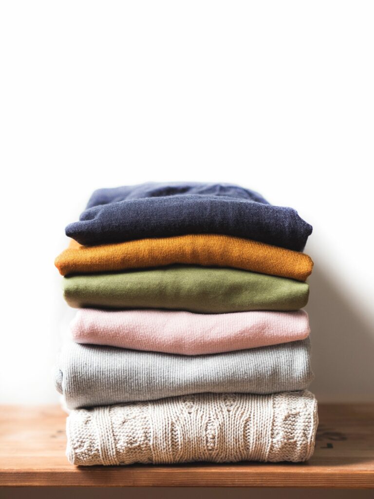 Pile of varicolored autumn clothes on wooden background, sweaters, knitwear, copy space